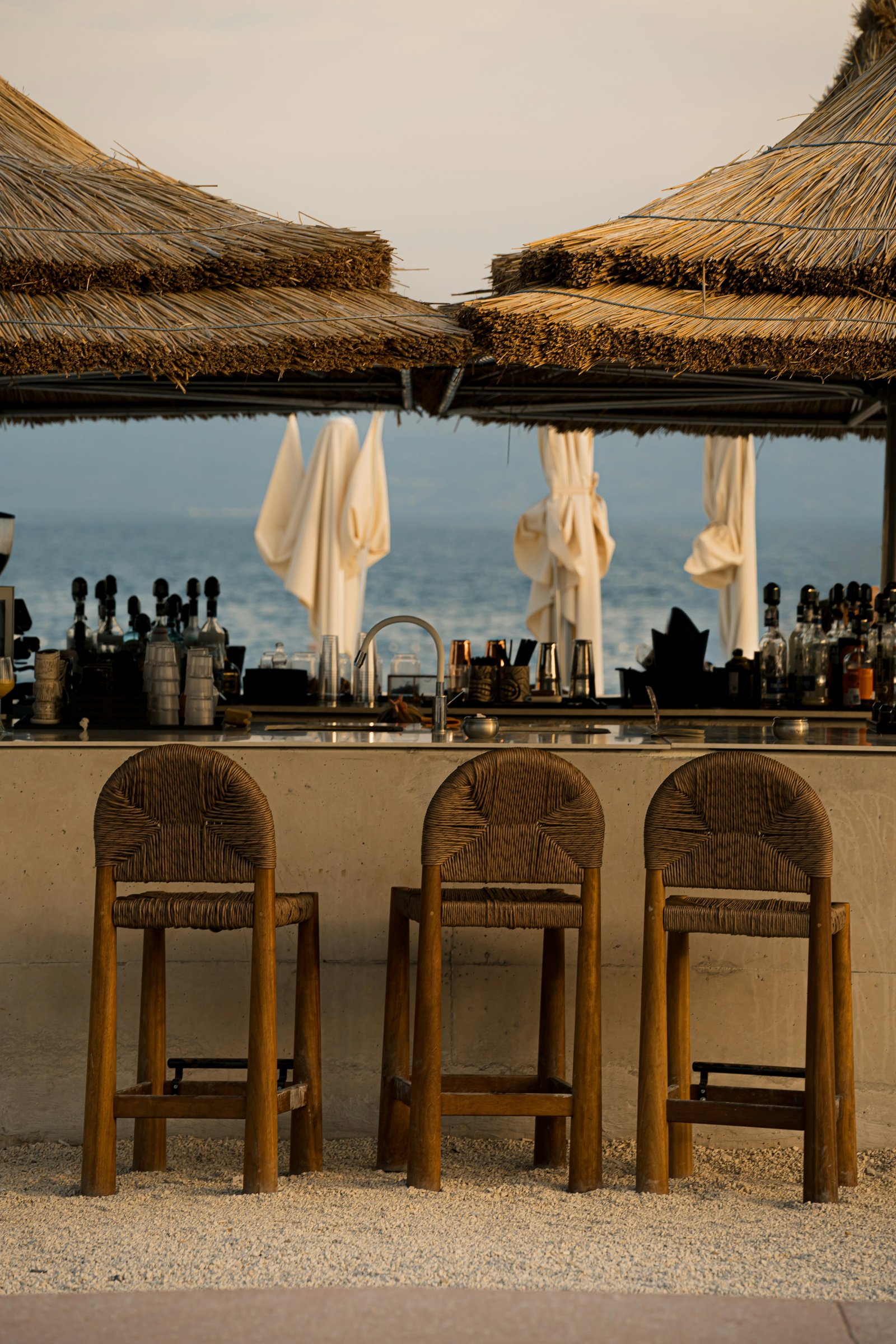 Taburetes de mimbre en una barra de playa con sombrillas de paja